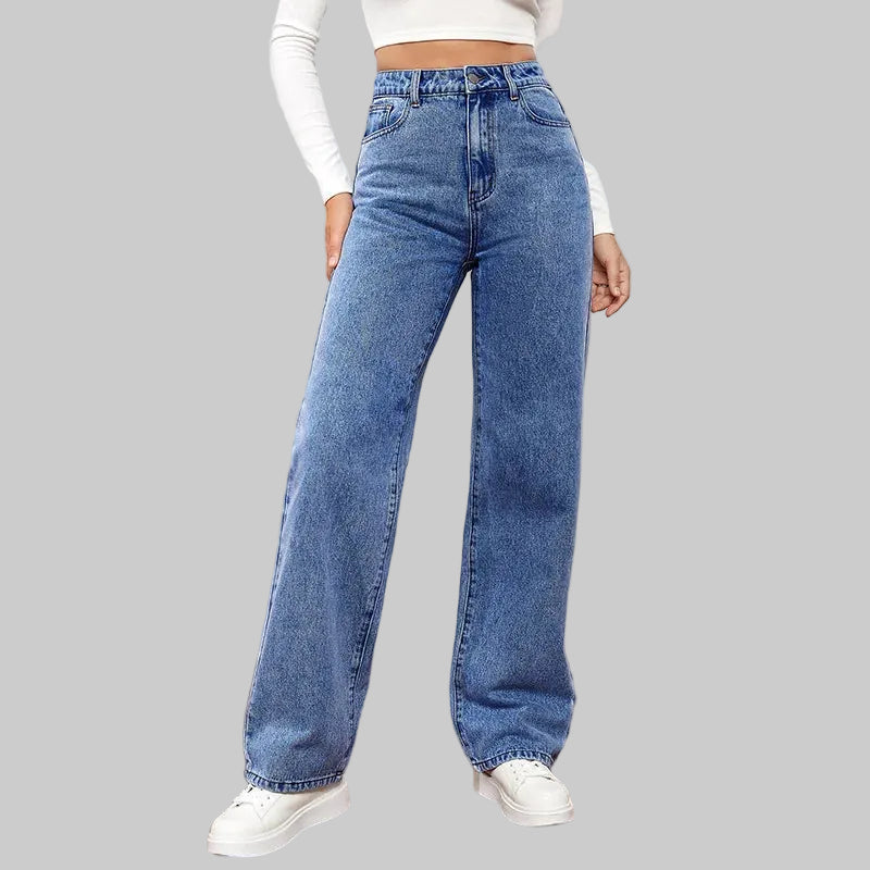 Person wearing blue jeans and white sneakers in a minimal indoor setting