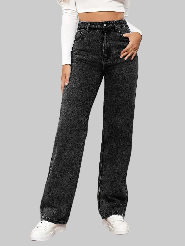 Person wearing black high-waisted jeans and white sneakers in a minimalistic room.
